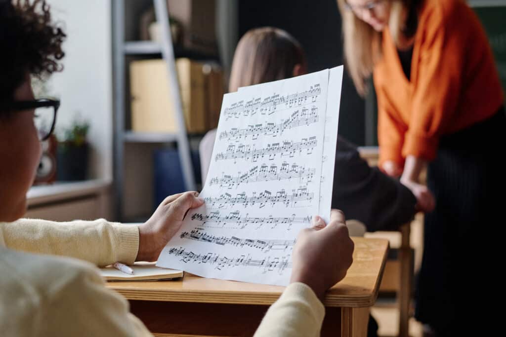 Selective focus shot of unrecognizable African American boy sitting at desk in classroom looking through sheet music paper during lesson