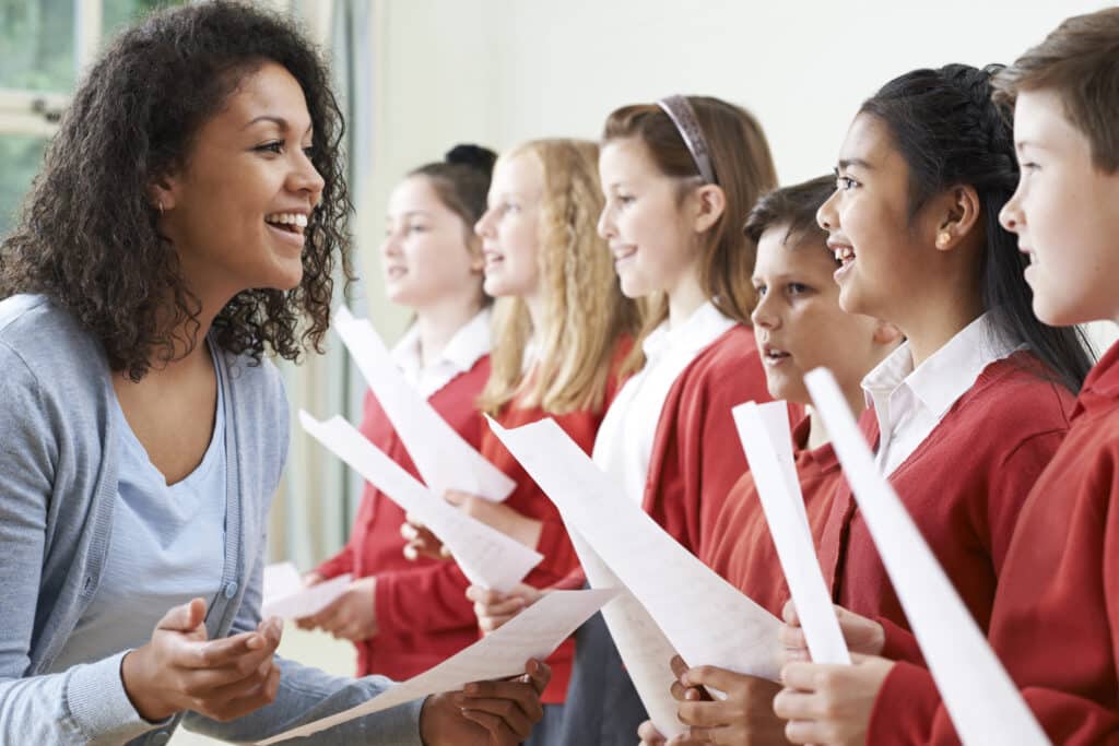 Children In School Choir Being Encouraged By Teacher